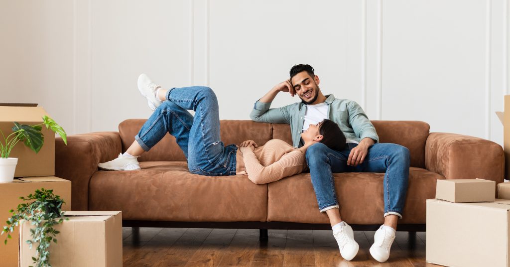 Two people sitting on a couch surrounded by moving boxes